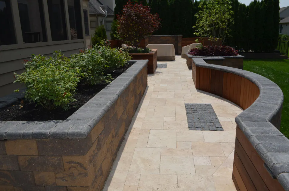 Raised segmental block planters with wood seat backs along a travertine-style walk